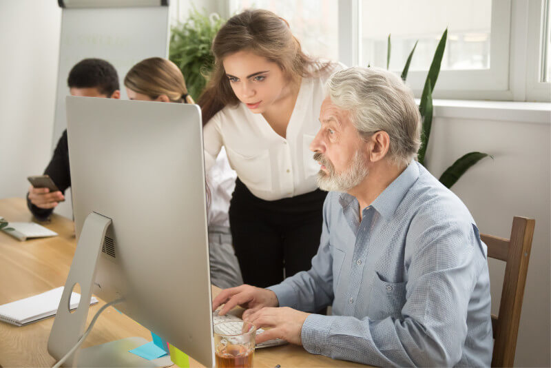 Trainerin hilft umschulenden Mann am Computer.